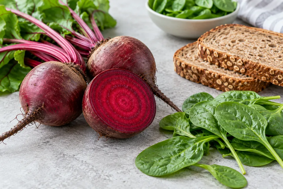 Whole and cut beetroot, spinach and whole-grain bread on a kitchen surface
